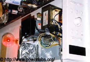 Microwave oven disassembled and layed out flat on a metal sheet. A neon globe is glowing ahead of it, with no electrical contact.